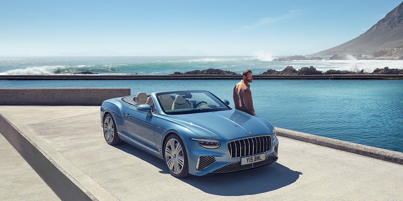 Bentley Tunbridge Wells New Bentley Continental GTC Azure convertible front view in Light Windsor blue paint with 22 inch ten spoke wheels parked by the sea in the sunshine