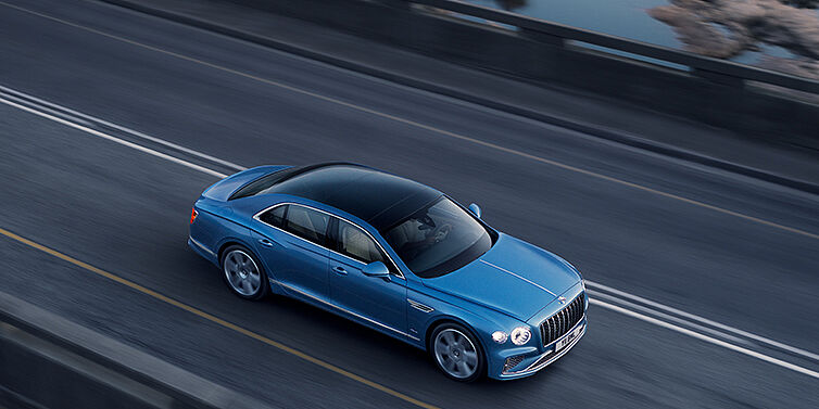 Bentley Tunbridge Wells New Bentley Flying Spur Azure sedan in Light windsor blue paint by Mulliner, with 22 inch Azure wheels seen from overhead driving dynamically on a country road
