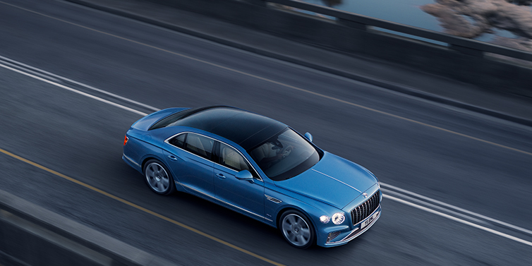 Bentley Tunbridge Wells New Bentley Flying Spur Azure sedan in Light windsor blue paint by Mulliner, with 22 inch Azure wheels seen from overhead driving dynamically on a country road